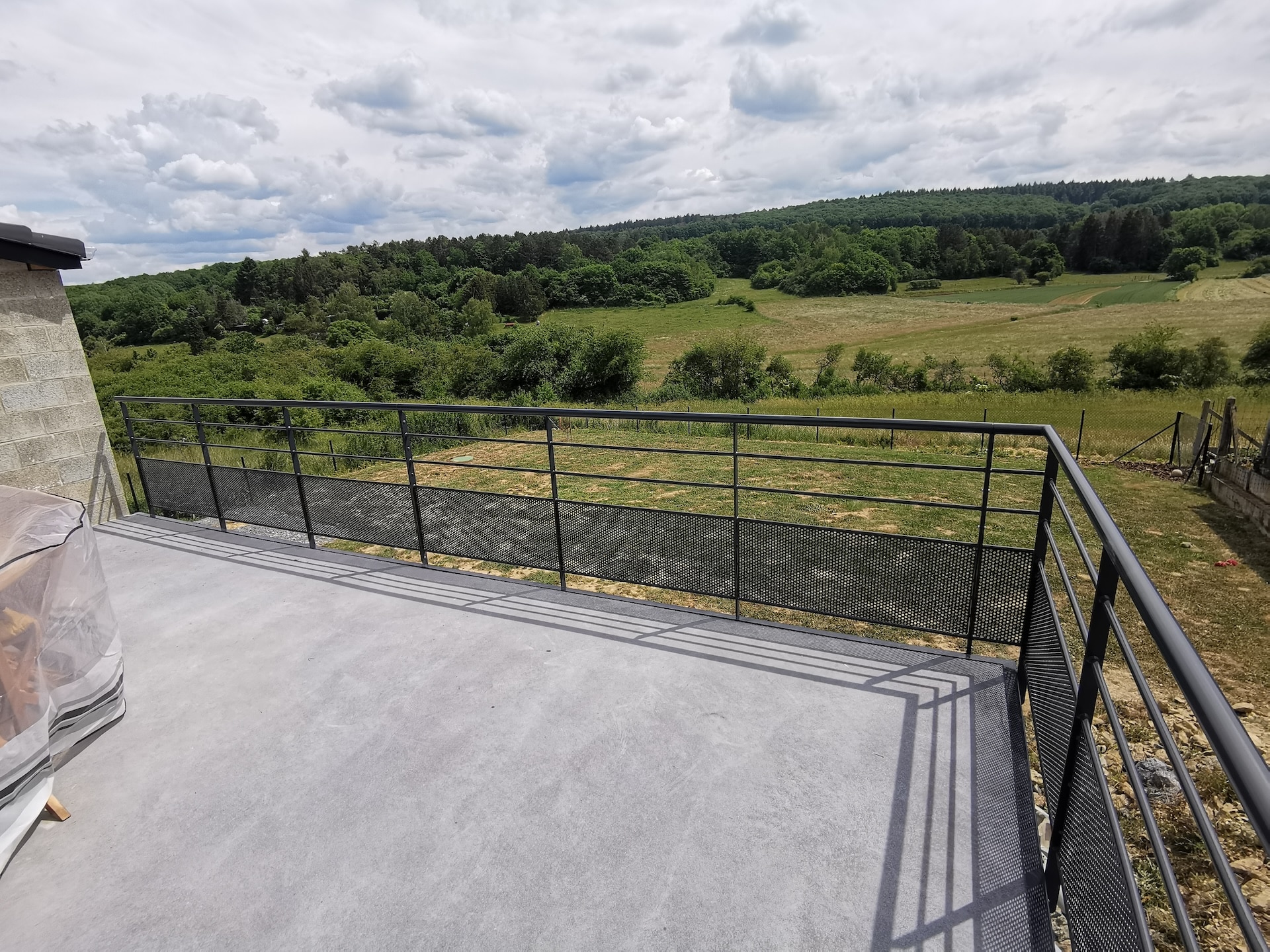 Terrasse moderne avec vue sur forêt et champs verts.